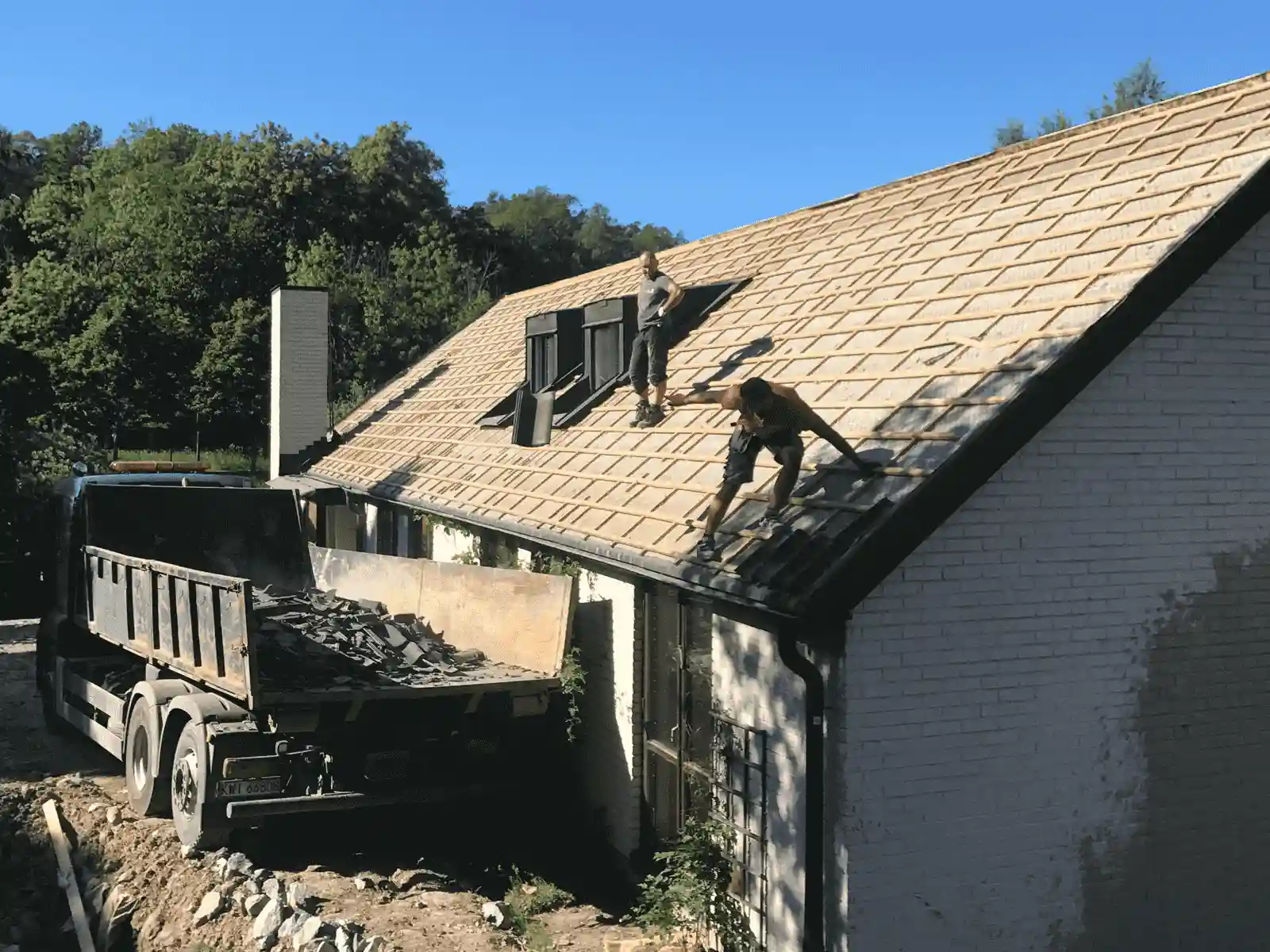 ett byggföretag river ett hus genom att ta bort takpannorna och lasta dem på en lastbil
