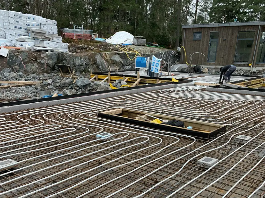 Fotot visar husets grund med armering utlagd, golvvärme och all rörmokeri redo för betonggjutning i Täby, Stockholm.